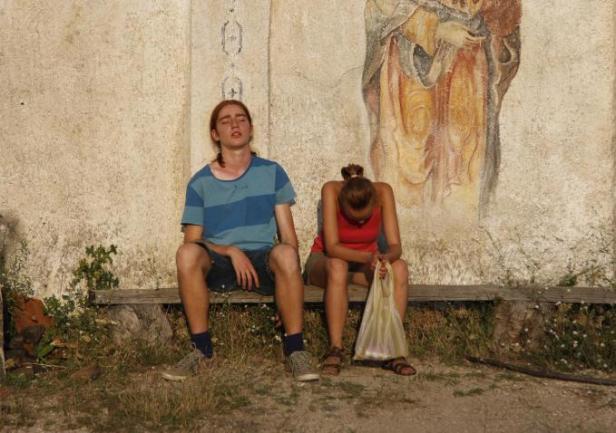The boy and the girl rest outside an abandoned church.